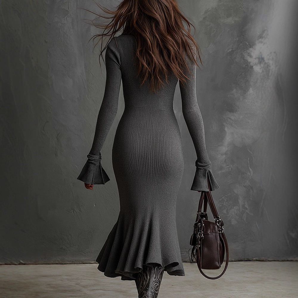 Woman in a gray dress holding a brown handbag against a textured gray wall.