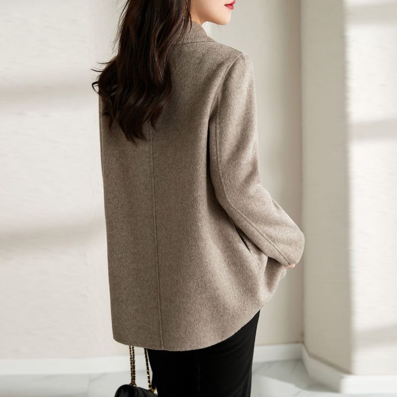 Person wearing a beige coat in a minimal indoor setting
