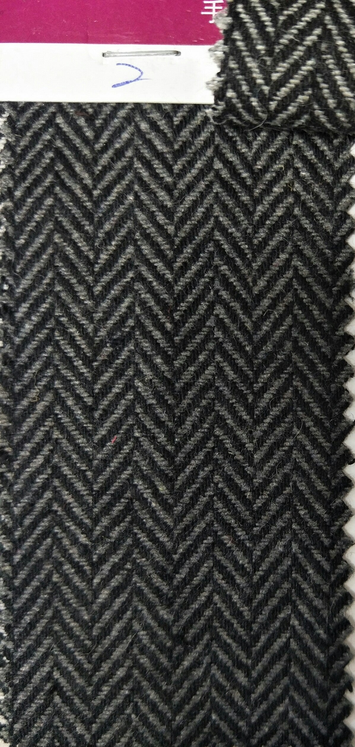 Herringbone pattern fabric swatch with a label on a pink background